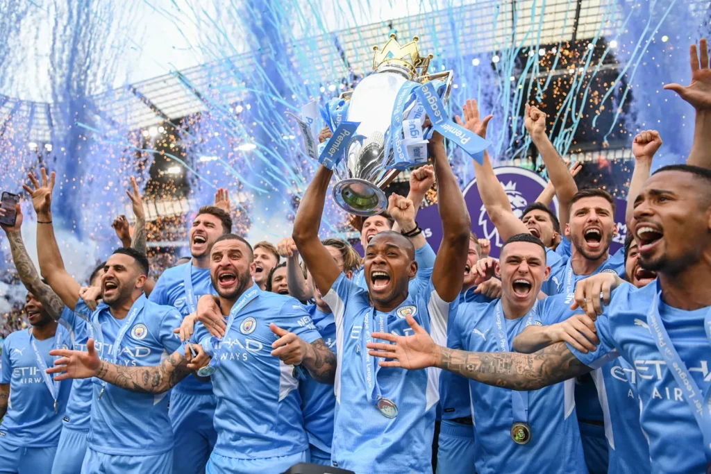 A imagem atual não possui texto alternativo. O nome do arquivo é: Manchester-City-Football-Club-team-celebrates-with-Premier-League-trophy-championship-May-22-2022-1.webp